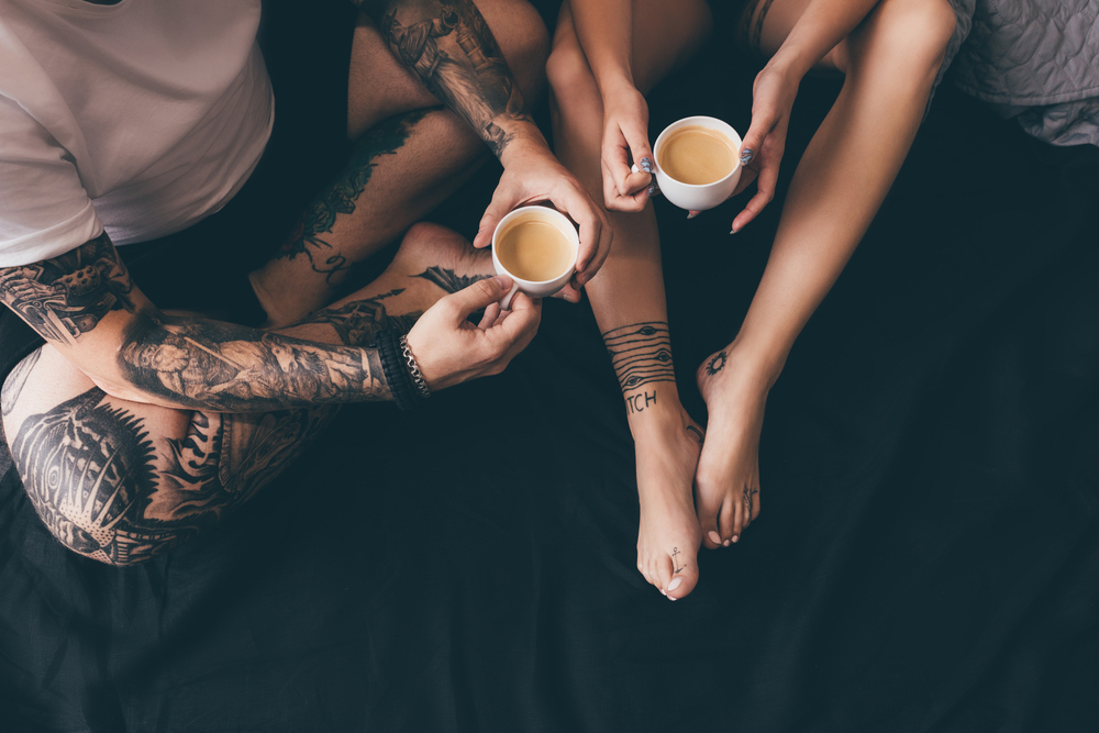 couple with tattoos drinking coffee and tea in bed