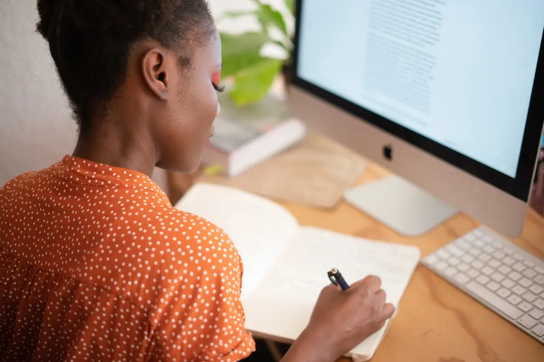 woman writing in notebook while working from home on computer